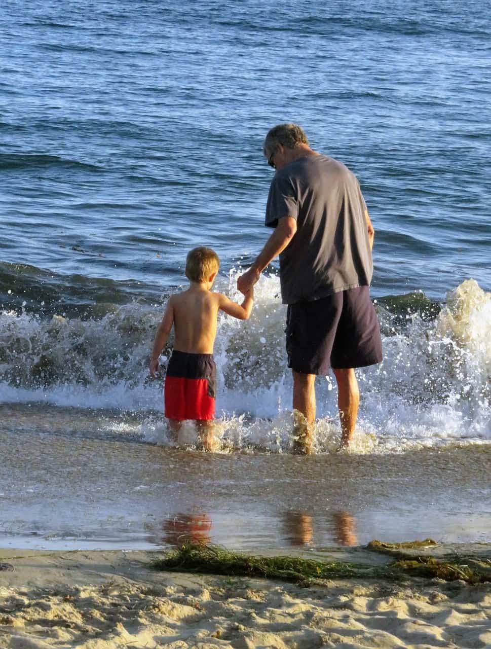 A man holding his grandson walking towards the sea.